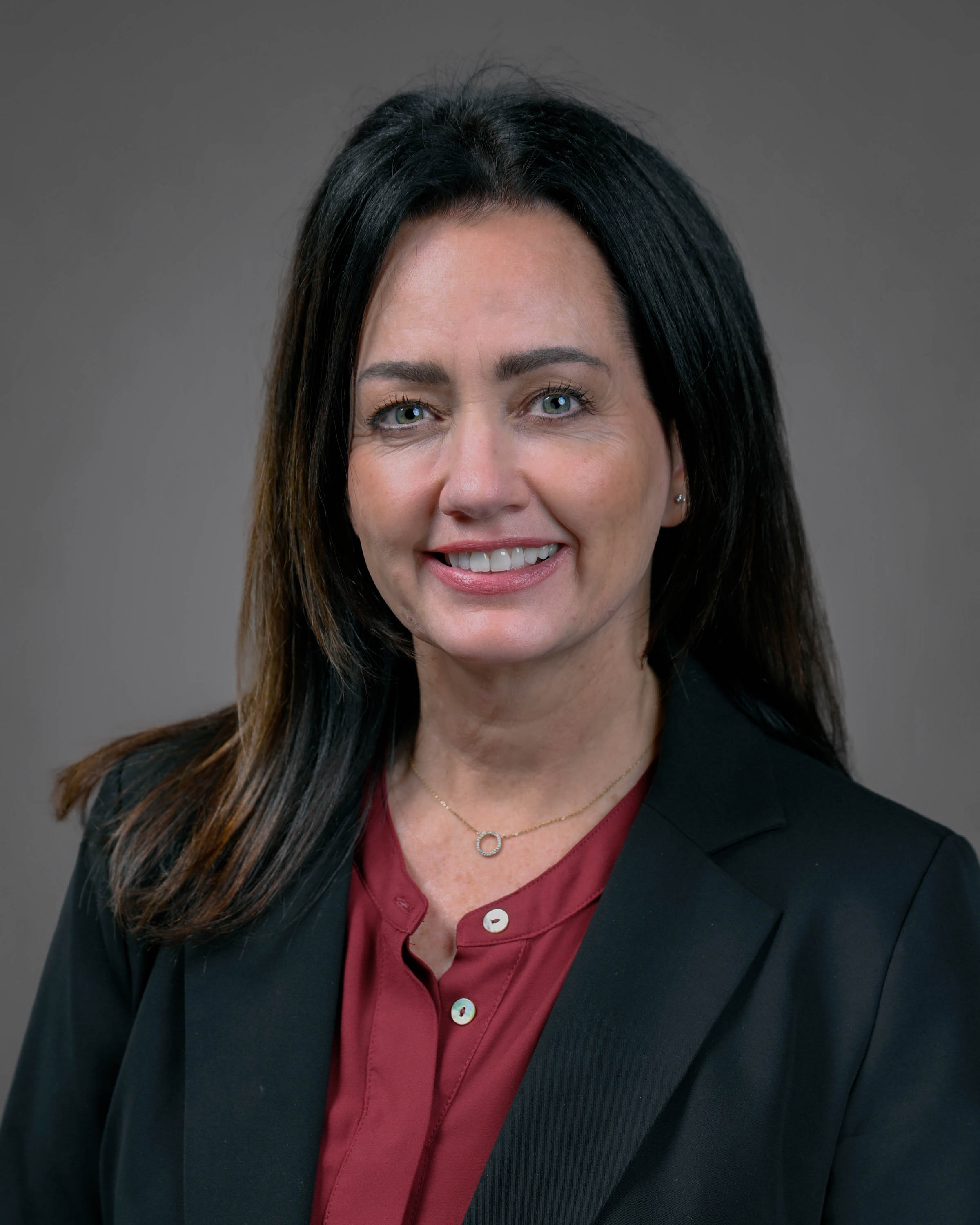 Smiling woman with long straight dark hair wearing a dark jacket and red shirt.